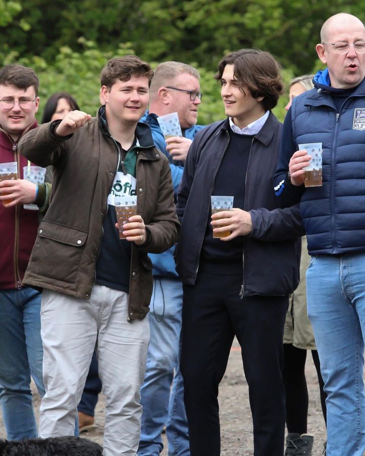 A crowd of festival-goers laugh and sing together, pints in hand
